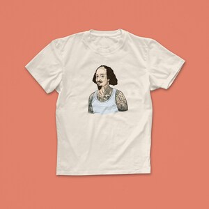 Pu&ograve; includere: Una maglietta bianca con una grafica di un uomo con la testa rasata e la barba, che indossa un canottiera bianca e tatuaggi sulle braccia.