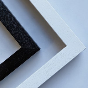 May include: Two picture frames, one black and one white, are shown with their corners overlapping. The frames are made of wood and have a simple, clean design.