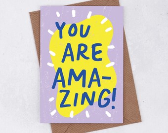 May include: A purple card with a yellow and white design. The card says "You are amazing!" in blue lettering.