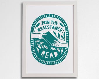May include: A teal blue and white framed print with a circular design. The design features a hand passing a book to another hand. The text reads "Join the Resistance: Read".