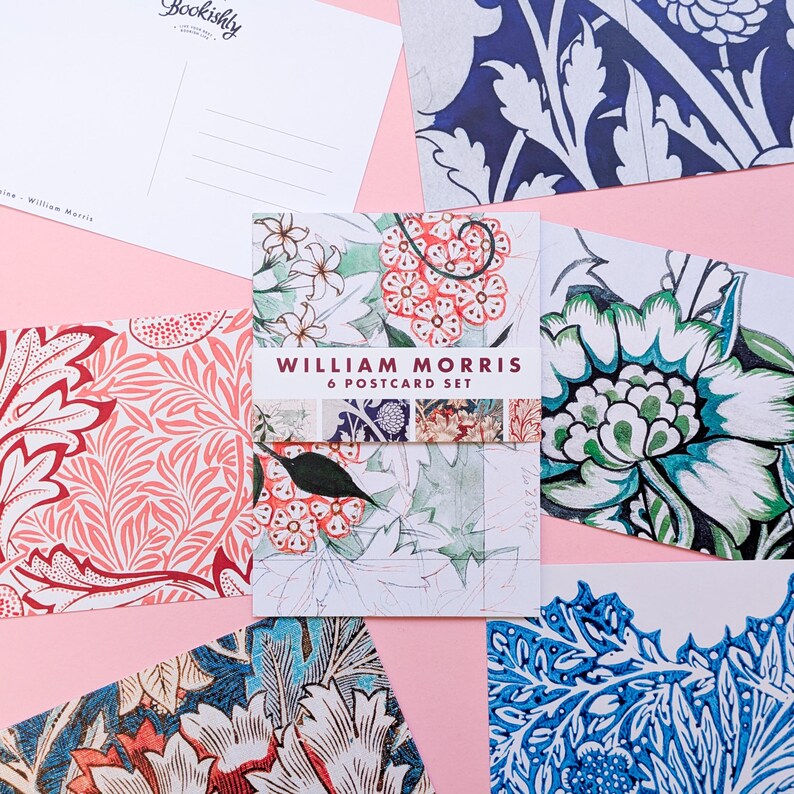 May include: A set of six William Morris postcards with floral designs in shades of red, blue, green, and white. The postcards are arranged on a pink background, with the words "William Morris 6 Postcard Set" printed on the front.