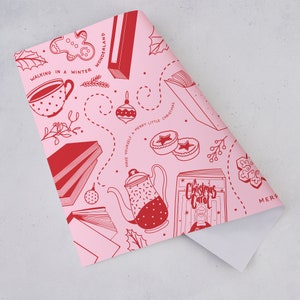 May include: Pink wrapping paper with a red and white Christmas themed pattern. The pattern includes books, teacups, ornaments, and a Christmas carol book.