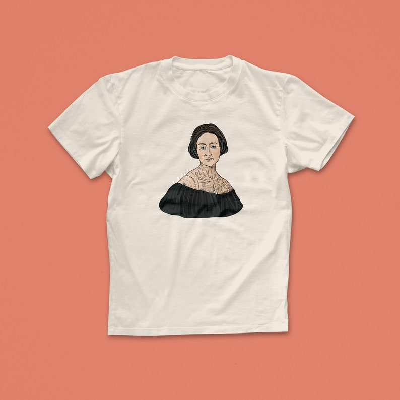 Pu&ograve; includere: Una maglietta bianca con un'illustrazione in bianco e nero di una donna con un tatuaggio sul petto.