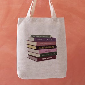 May include: A beige tote bag with cream-coloured handles. The bag features a stack of books with titles like "Pride and Prejudice" and "Mansfield Park." The text "THE WORKS OF JANE AUSTEN" is also visible.