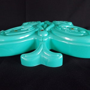 May include: A teal blue butterfly-shaped plastic trinket box with a raised design. The box is closed and has a small gold accent on the top.