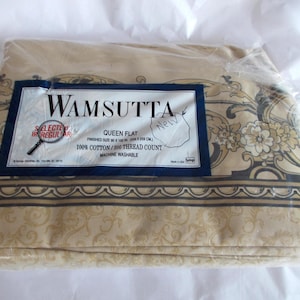 May include: A beige Wamsutta Queen flat sheet set, still in its original packaging. The sheet set features a floral and scroll design with a dark border. The label reads "Selected Irregular" and includes the text "100% Cotton/200 Thread Count".