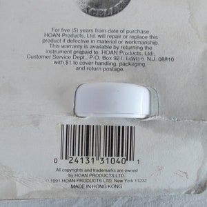 Op de afbeelding: Een wit plastic product met een barcode en tekst die luidt: "Voor vijf (5) jaar vanaf de aankoopdatum. HOAN Products. Ltd. zal dit product repareren of vervangen als het defect is in materiaal of afwerking. Deze garantie is beschikbaar door het instrument per vooruitbetaling terug te sturen naar: HOAN Products, Ltd.. Klantenservice, Postbus 921. Dayton N.J. 08810 met $ 1 voor afhandeling, verpakking en retourzending. 0 24131 31040 1 Alle auteursrechten en handelsmerken zijn eigendom van HOAN PRODUCTS LTD. 1991 HOAN PRODUCTS LTD. New York 11232 GEMAAKT IN HONGKONG"