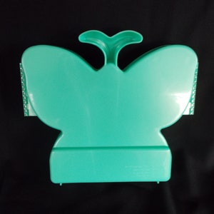 May include: A teal plastic butterfly-shaped storage box with a hinged lid. The box has a small handle on top and a textured design on the sides.