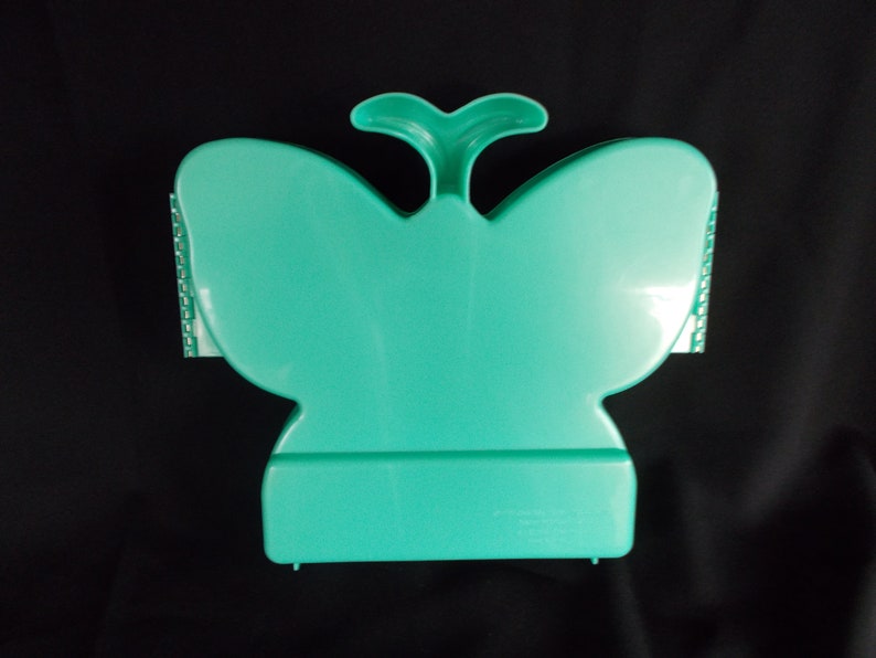 May include: A teal plastic butterfly-shaped storage box with a hinged lid. The box has a small handle on top and a textured design on the sides.