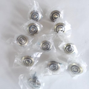 May include: A collection of new, antique brass-colored cabinet knobs, each individually wrapped in clear plastic. The knobs have a circular design with a recessed center and a decorative edge.