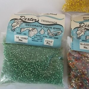May include: Bags of Dexter's Trimmings, featuring small, colorful beads. The bags have a light blue label with illustrations and text that reads "Decorate Your Own." The labels also include the text "Dresses, Hats, Belts, Shoes, Veils, Sweaters, Headbands, etc."