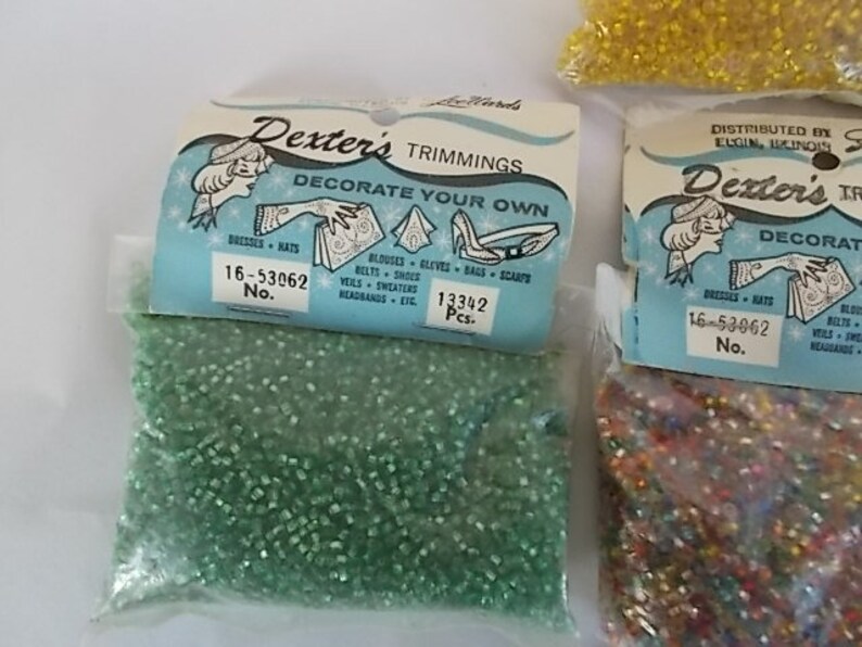 May include: Bags of Dexter's Trimmings, featuring small, colorful beads. The bags have a light blue label with illustrations and text that reads "Decorate Your Own." The labels also include the text "Dresses, Hats, Belts, Shoes, Veils, Sweaters, Headbands, etc."