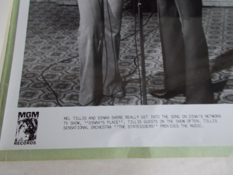 May include: Black and white photo of Mel Tillis and Dinah Shore singing together on Dinah's Place. The caption reads "Mel Tillis and Dinah Shore really get into the song on Dinah's network TV show, 'Dinah's Place'. Tillis is guests on the show often. Tillis Sensational Orchestra 'The Statesiders' provides the music."