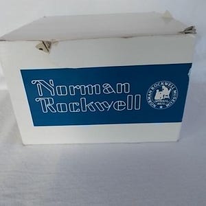 May include: A white box with a blue label that says "Norman Rockwell" and features a logo for the Norman Rockwell Museum.