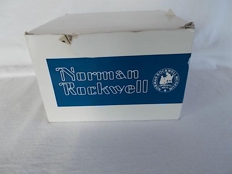 May include: A white box with a blue label that says "Norman Rockwell" and features a logo for the Norman Rockwell Museum.