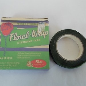 May include: A roll of dark green floral stem tape next to a box of Floral-Wrap stemming tape. The box is green with a red rose illustration and the text "Floral-Wrap Stemming Tape". The box also says "roll of 60 ft."