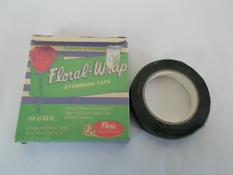May include: A roll of dark green floral stem tape next to a box of Floral-Wrap stemming tape. The box is green with a red rose illustration and the text "Floral-Wrap Stemming Tape". The box also says "roll of 60 ft."