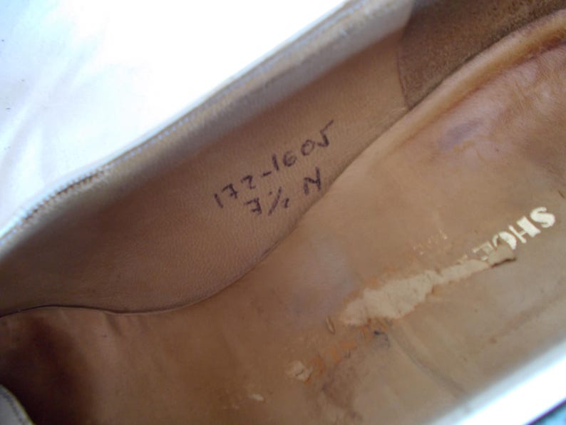 May include: Interior view of a shoe, showing the insole with handwritten markings. The markings include the numbers "172-1605" and "7 1/2 N". The shoe's interior is a light tan color.