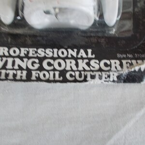 Op de afbeelding: Een professionele vleugelkurkentrekker van wit plastic met een folie-snijder. De verpakking is zwart met witte tekst die "Professional Wing Corkscrew with Foil Cutter" en "Style No. 31040" luidt.