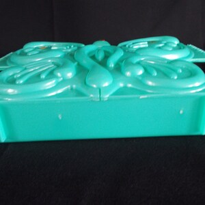 May include: A teal plastic box with a decorative butterfly design on the lid. The box is closed and the lid is slightly ajar.