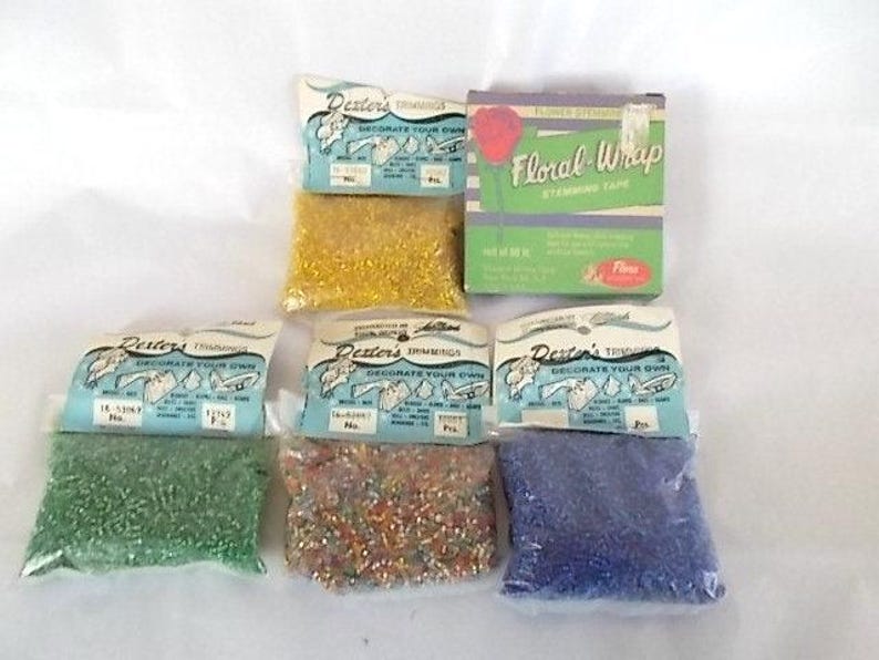 May include: A collection of craft supplies including four small plastic bags of colorful beads in green, gold, multi-color, and blue, each with a Dexter's Trimmings label, and one green box labeled Floral-Wrap Stemming Tape with a red rose graphic.