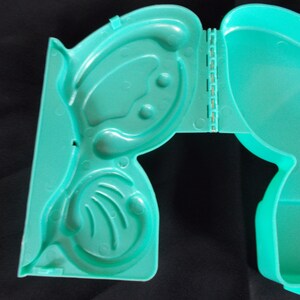 May include: A teal plastic hinged box with a molded design of a butterfly. The box is open and the inside is visible.