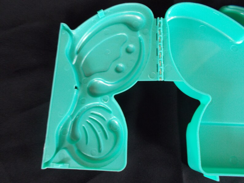 May include: A teal plastic hinged box with a molded design of a butterfly. The box is open and the inside is visible.