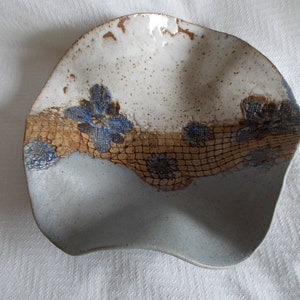 May include: A ceramic bowl with a white glaze and brown and blue floral designs. The bowl has a wavy edge and a light blue glaze on the bottom.