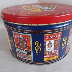 Op de afbeelding: Een ronde blikken doos in blauw en rood met het Quaker Oats logo op de deksel. De zijkanten van de doos tonen afbeeldingen van het Quaker Oats logo, het Buckeye Rolled Oats logo en de tekst "Rolled White Oats".