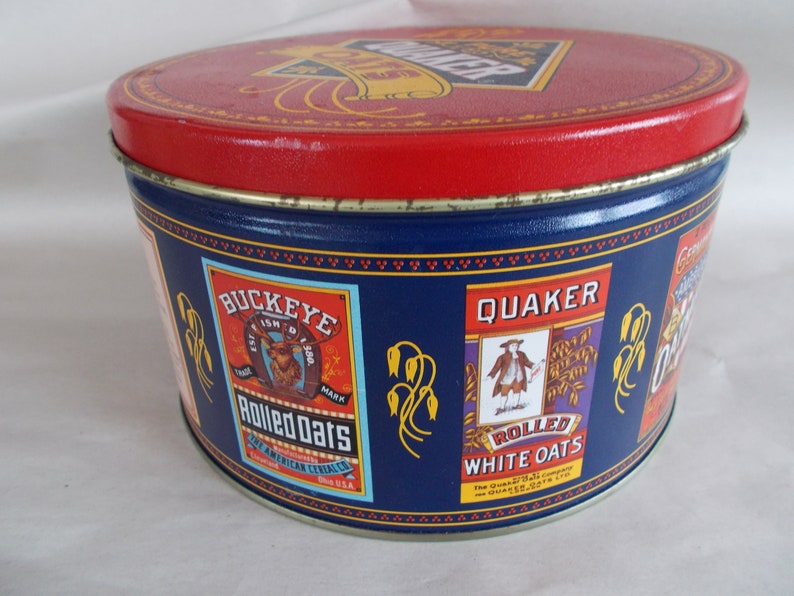 Op de afbeelding: Een ronde blikken doos in blauw en rood met het Quaker Oats logo op de deksel. De zijkanten van de doos tonen afbeeldingen van het Quaker Oats logo, het Buckeye Rolled Oats logo en de tekst "Rolled White Oats".