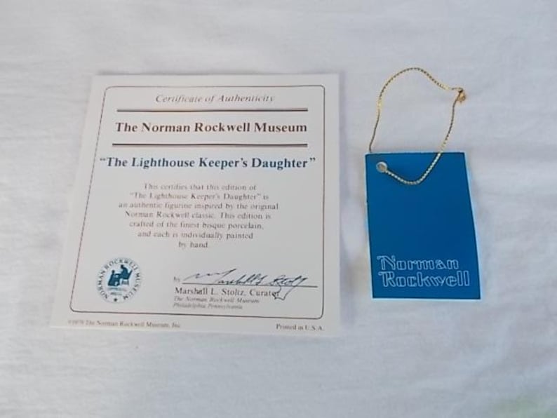 May include: A certificate of authenticity for a porcelain figurine of "The Lighthouse Keeper's Daughter" by Norman Rockwell. The certificate is printed on white paper with blue and gold accents. The certificate is signed by Marshall L. Stoltz, Curator of the Norman Rockwell Museum.