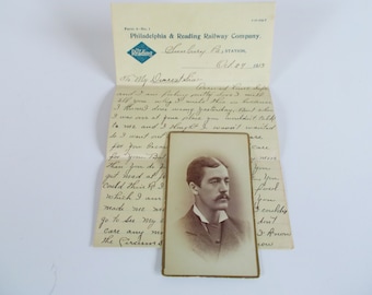 May include: A vintage black and white photograph of a man with a mustache, wearing a suit and tie. The photo is mounted on a card with a gold border. The card is folded in half and has a handwritten letter on the back. The letter is dated October 27, 1915, and is addressed to "My Dearest Sis".
