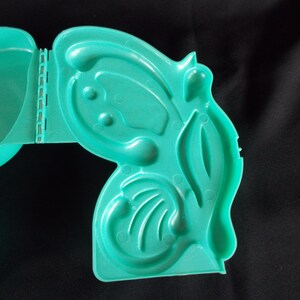 May include: A teal blue plastic mold with multiple compartments, shaped like a butterfly. The mold is open and ready to be used.