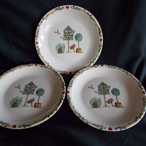 May include: Set of three white ceramic salad plates with a green birdhouse design. The plates have a yellow and green border with red hearts.
