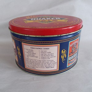 Op de afbeelding: Een blauwe en rode blikken container met een Quaker Oats logo op de deksel. De zijkant van de blik heeft een recept voor beroemde haverkoekjes. Het recept bevat ingredi&euml;nten zoals bakvet, bruine suiker, havervlokken, bloem en vanille. De blik heeft ook een Buckeye's Adventure logo.
