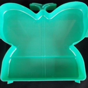 May include: A teal plastic butterfly-shaped container with a hinged lid. The container has a divided interior.