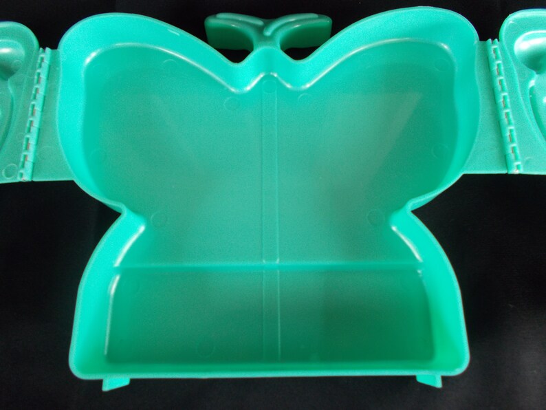May include: A teal plastic butterfly-shaped container with a hinged lid. The container has a divided interior.