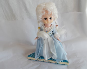 May include: A vintage doll with a white wig and blue dress, sitting on a box with the text "FIRST LADY - 178".