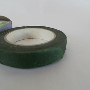 May include: A roll of dark green floral tape with a white inner core. The tape is partially unrolled, revealing the adhesive side. A portion of a box is visible in the background.