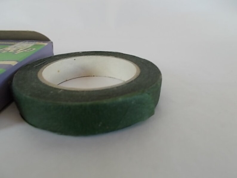 May include: A roll of dark green floral tape with a white inner core. The tape is partially unrolled, revealing the adhesive side. A portion of a box is visible in the background.