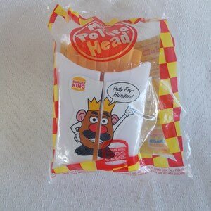 May include: A sealed plastic bag containing a Mr. Potato Head toy with a Burger King theme. The bag features a cartoon image of Mr. Potato Head holding a fry container with the text "Indy Fry-Hundred". The bag has a red and yellow checkered pattern.