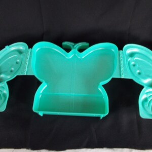 May include: A teal plastic butterfly-shaped box with a hinged lid. The box is divided into three sections.