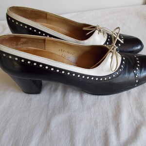May include: A pair of vintage black and white leather shoes with a low heel. The shoes have a classic design with a white accent on the top and a lace-up closure. The shoes are in good condition.