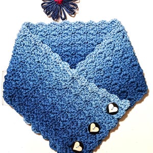 May include: A blue crocheted cowl with a gradient effect, transitioning from light to dark shades. The cowl features three heart-shaped buttons and a decorative blue flower. This handmade accessory is perfect for adding a touch of handmade charm to any outfit.