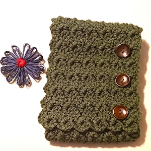 May include: An olive green crocheted sleeve with three brown buttons. A blue and red decorative flower is to the left of the sleeve. The sleeve has a textured pattern and a scalloped edge.