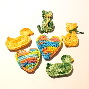 May include: A collection of handmade crochet items, including two heart shapes, two duck shapes, and two cat shapes. The items are in various colors, such as orange, green, blue, and yellow. The items are made of yarn.