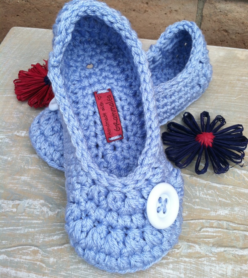 May include: A pair of light blue crocheted slippers with a white button on each. The slippers have a label that says "Handmade with love by Grammadel".