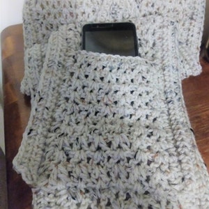 Pode incluir: Uma echarpe de croch&ecirc; branca com um bolso para o telefone. O bolso &eacute; feito com um padr&atilde;o de ponto diferente do resto da echarpe.