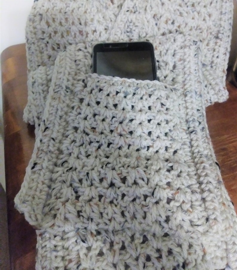 Pode incluir: Uma echarpe de croch&ecirc; branca com um bolso para o telefone. O bolso &eacute; feito com um padr&atilde;o de ponto diferente do resto da echarpe.