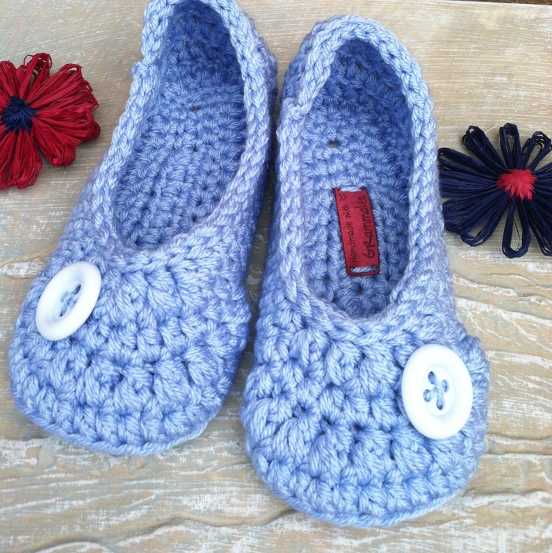 May include: A pair of light blue crocheted slippers with white buttons. The slippers are handmade and have a label that says "Handmade with love by Grammie".